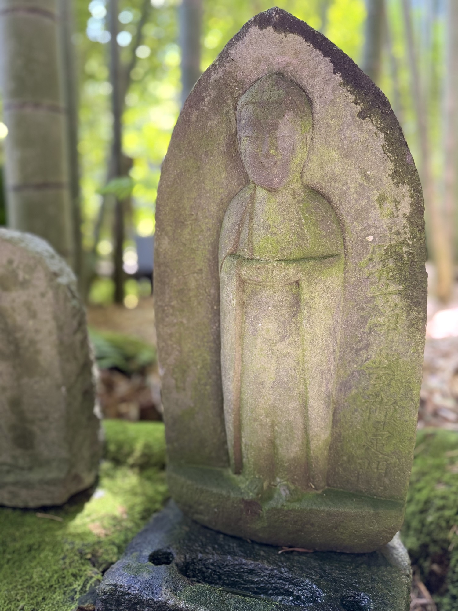 A moss-covered stone Jizō statue in a bamboo garden